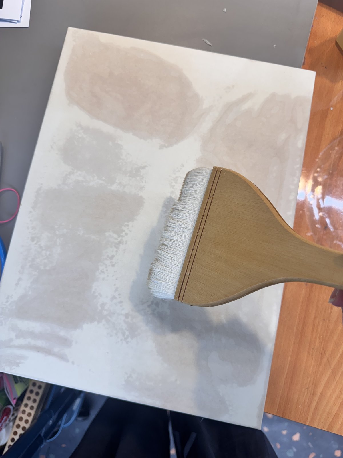 A wide hake brush sizing a panel with water.